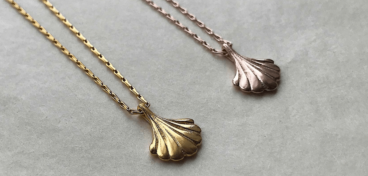 A gold and rose gold wing necklace both featuring the art deco scallop theme