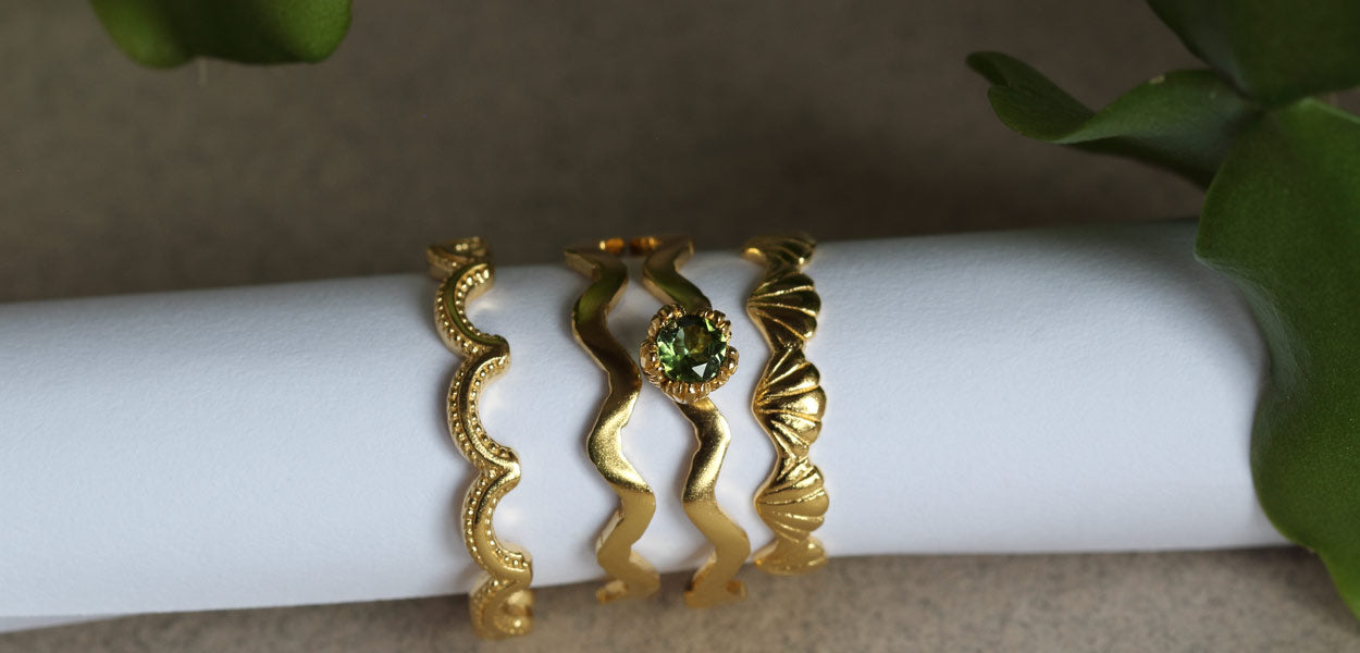 Four intricately textured gold stacking rings, one set with a beautiful green tourmaline gemstone