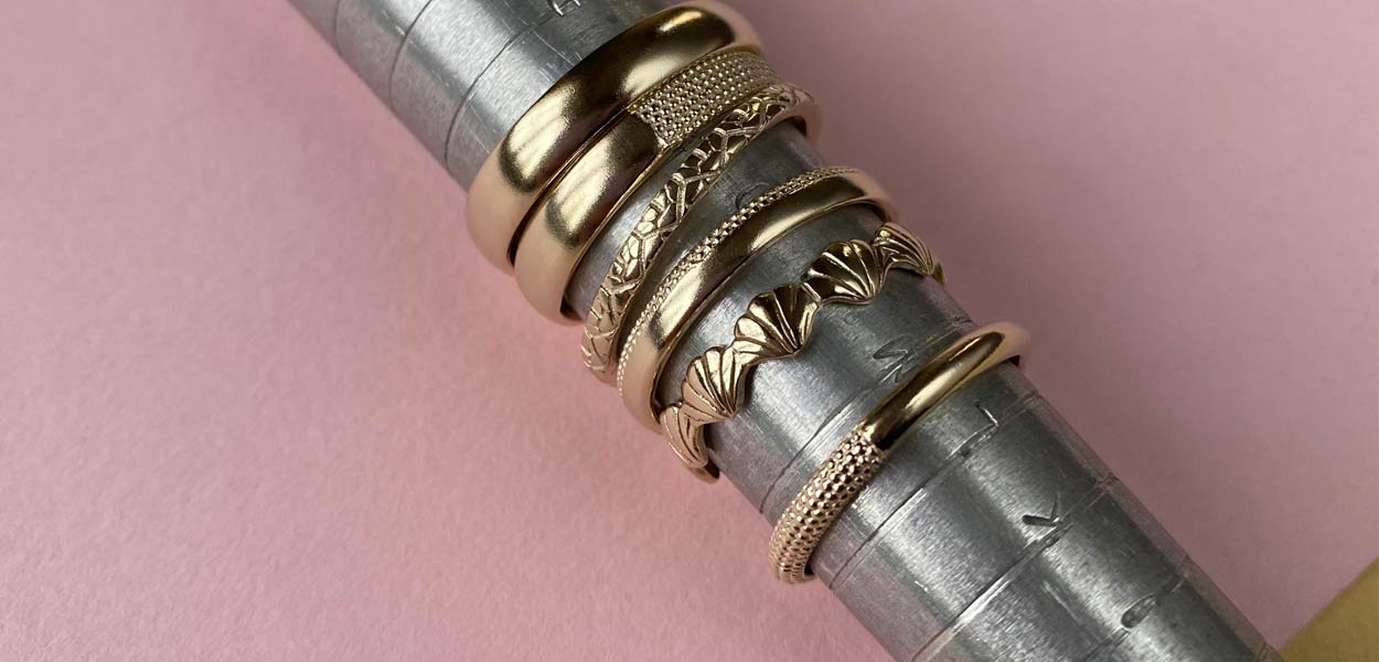 Six solid gold patterned wedding bands on a measuring ring stick 