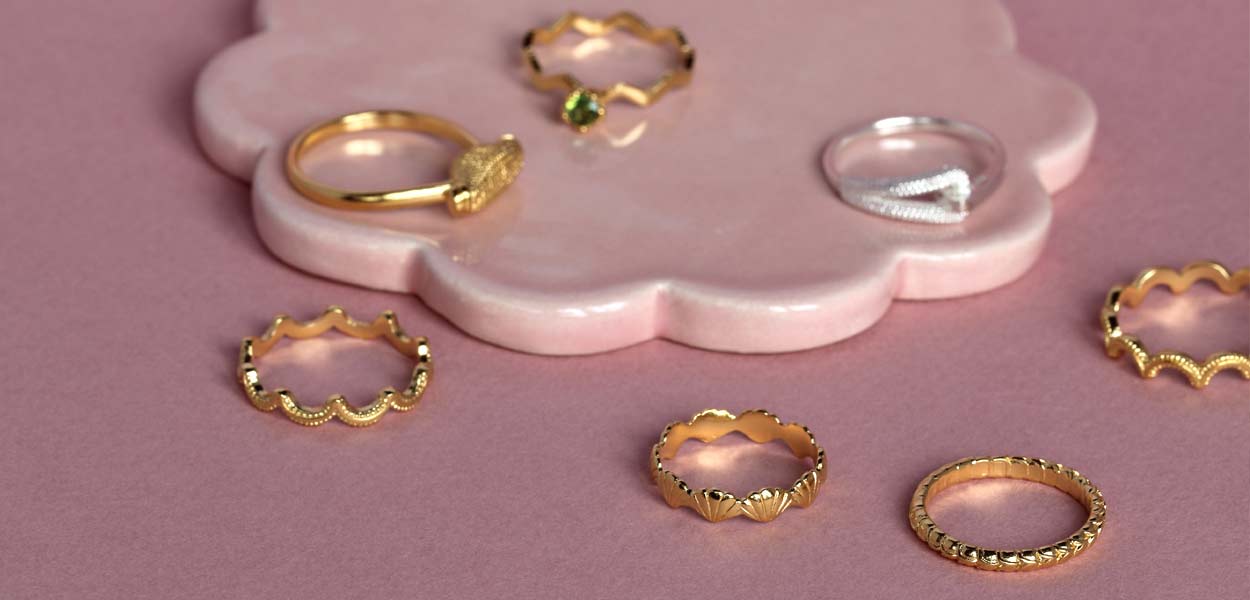 6 gold and 1 silver pinkie rings neatly arranged on pink background