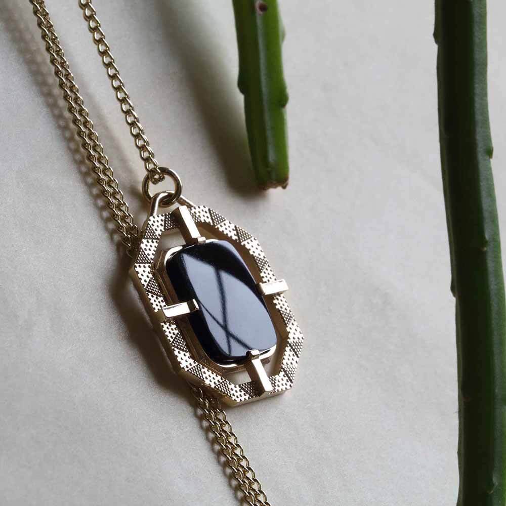 Bespoke onyx pendant with triangular patterned and chain shot next to succulent plant