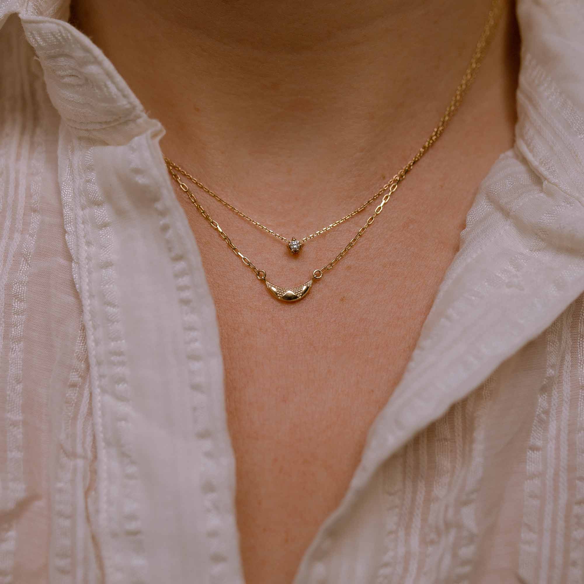 Model wears tiny diamond necklace layered with textured crescent moon necklace