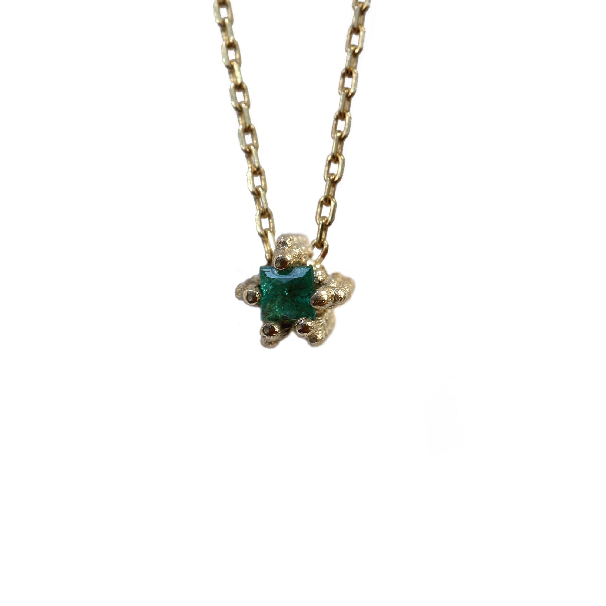 Tiny square cut emerald set in textured gold necklace on white background