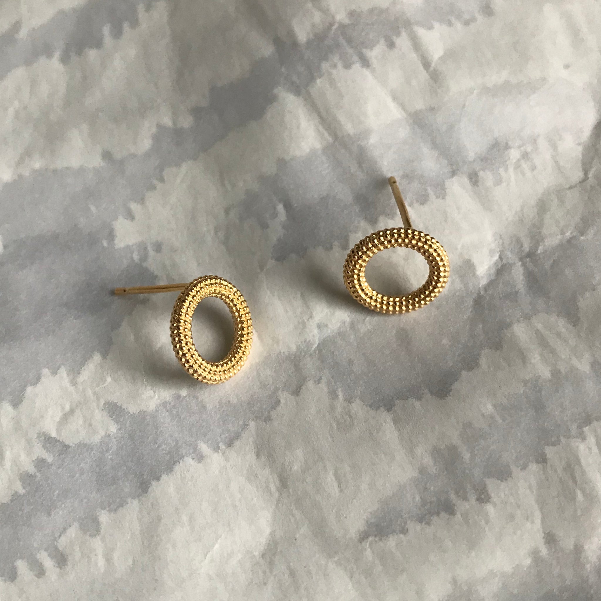 A pair of donut shaped yellow gold stud earrings with dot texture