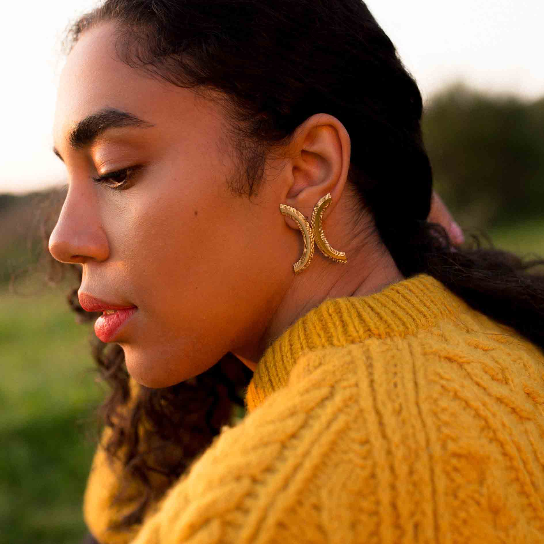 Model in yellow jumper wearing 2 crescent gold earrings
