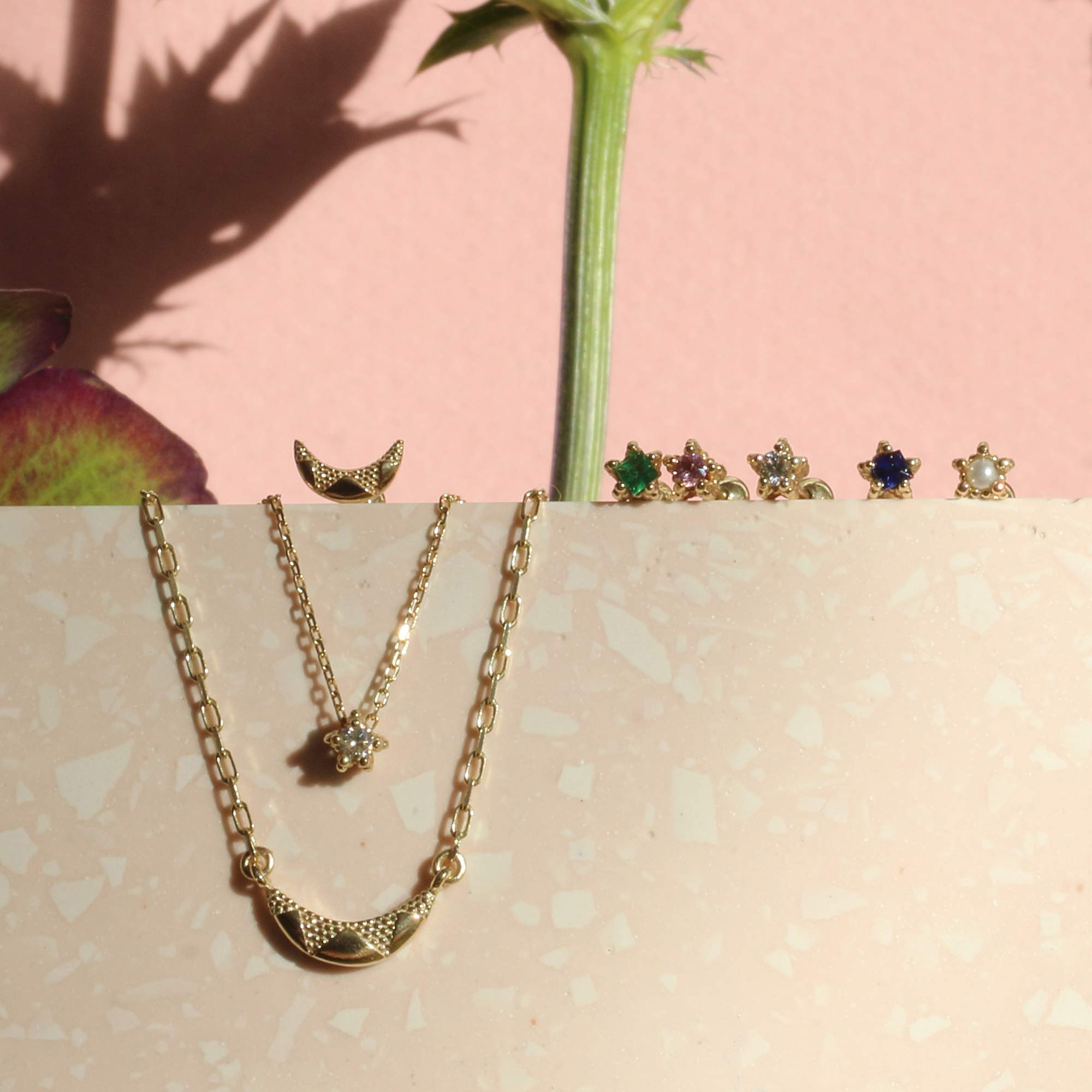Line up of textured 9ct gold gemstone earrings and necklaces on pink backdrop