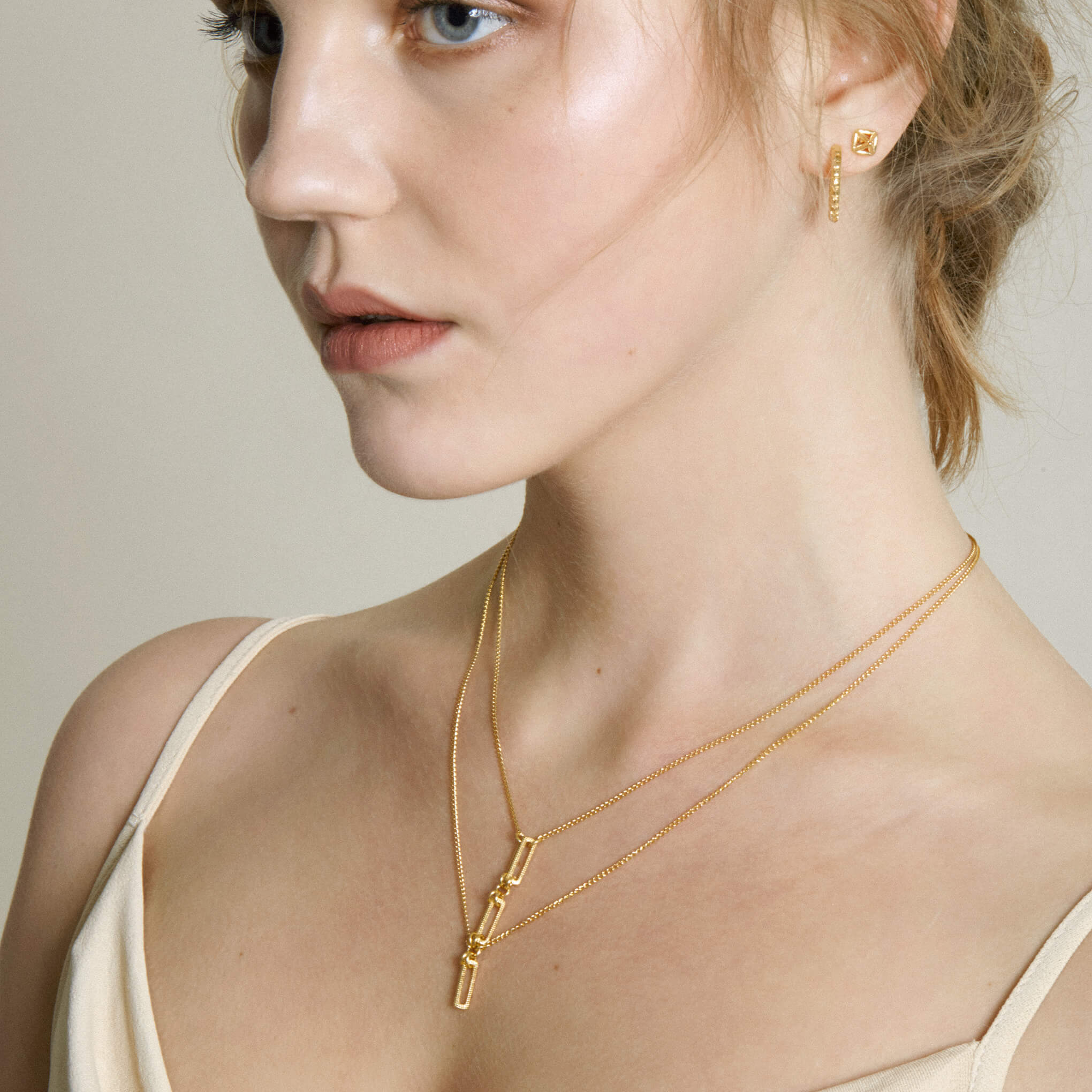 A model wearing a gold necklace and hoop and pyramid stud earrings