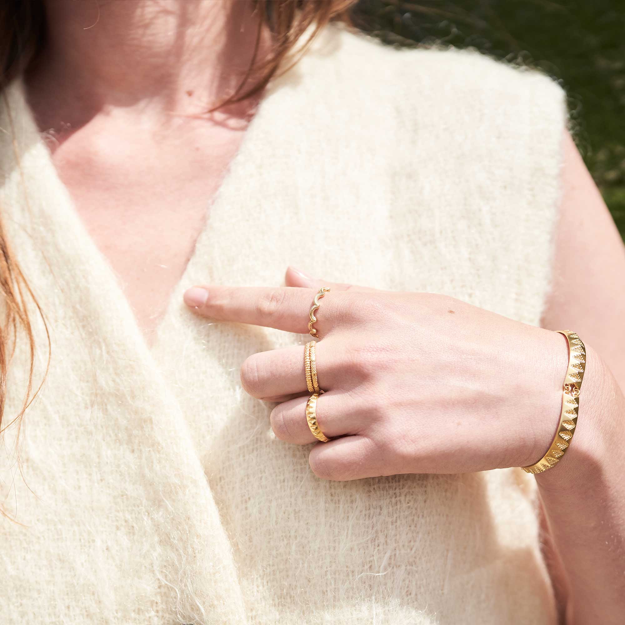 A model in a white wool top wearing gold rings and bracelet