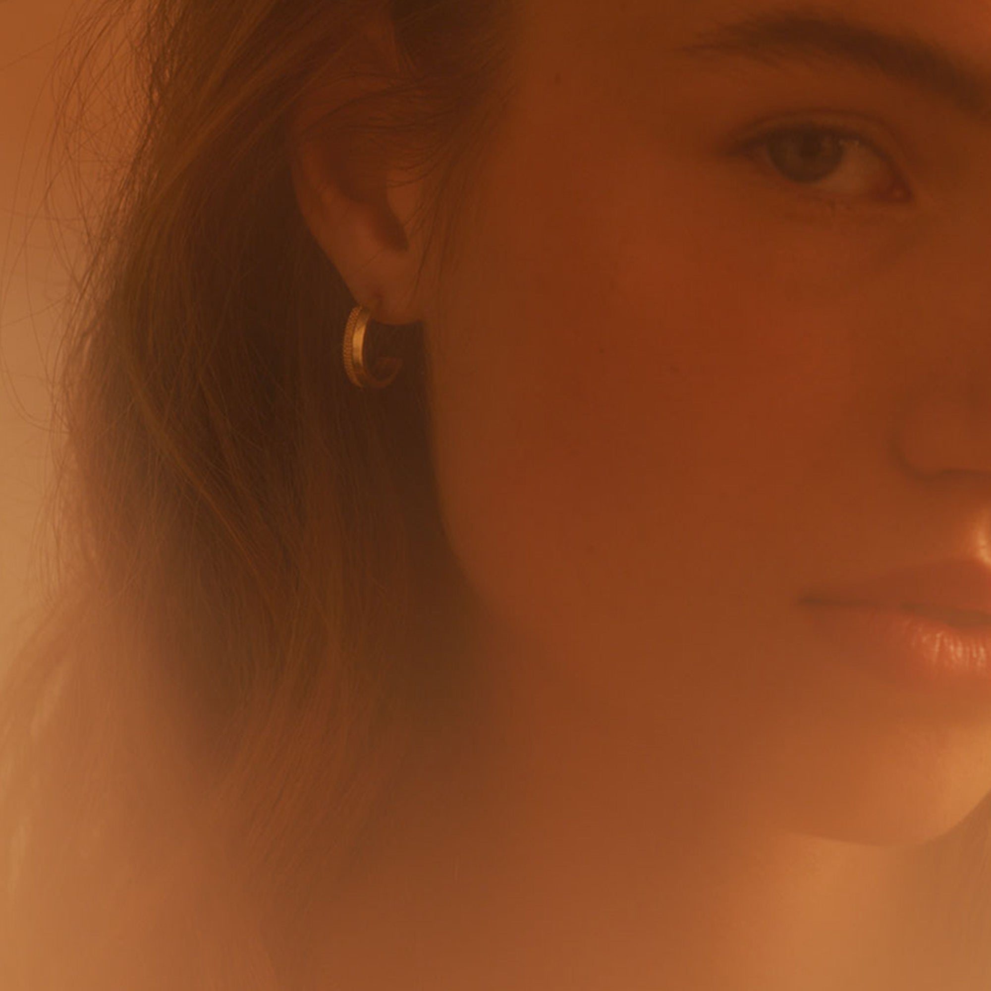 A model looking through hazy light wearing a gold hoop earringarrings