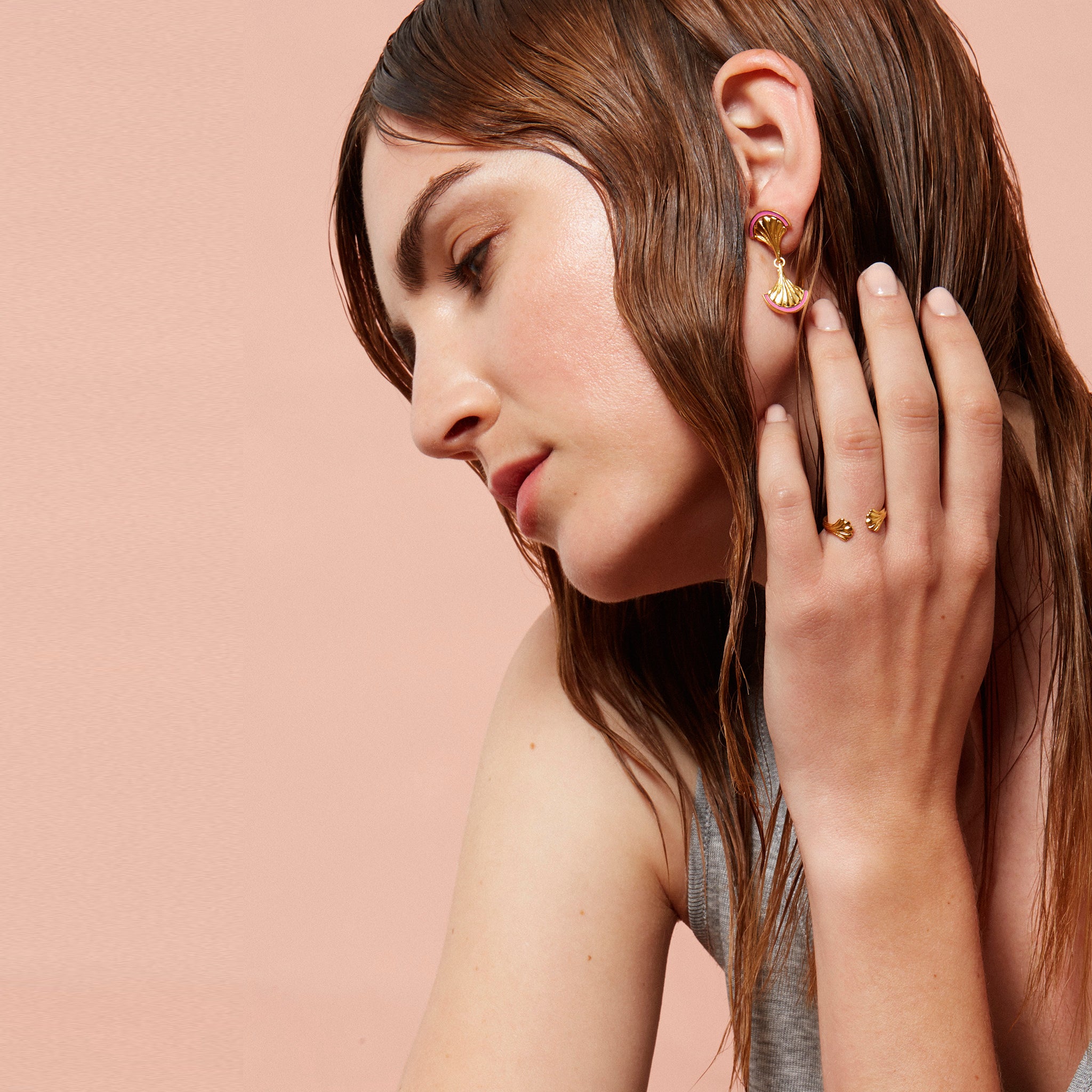 A lady wearing gold drop earrings with pink enamel detailing
