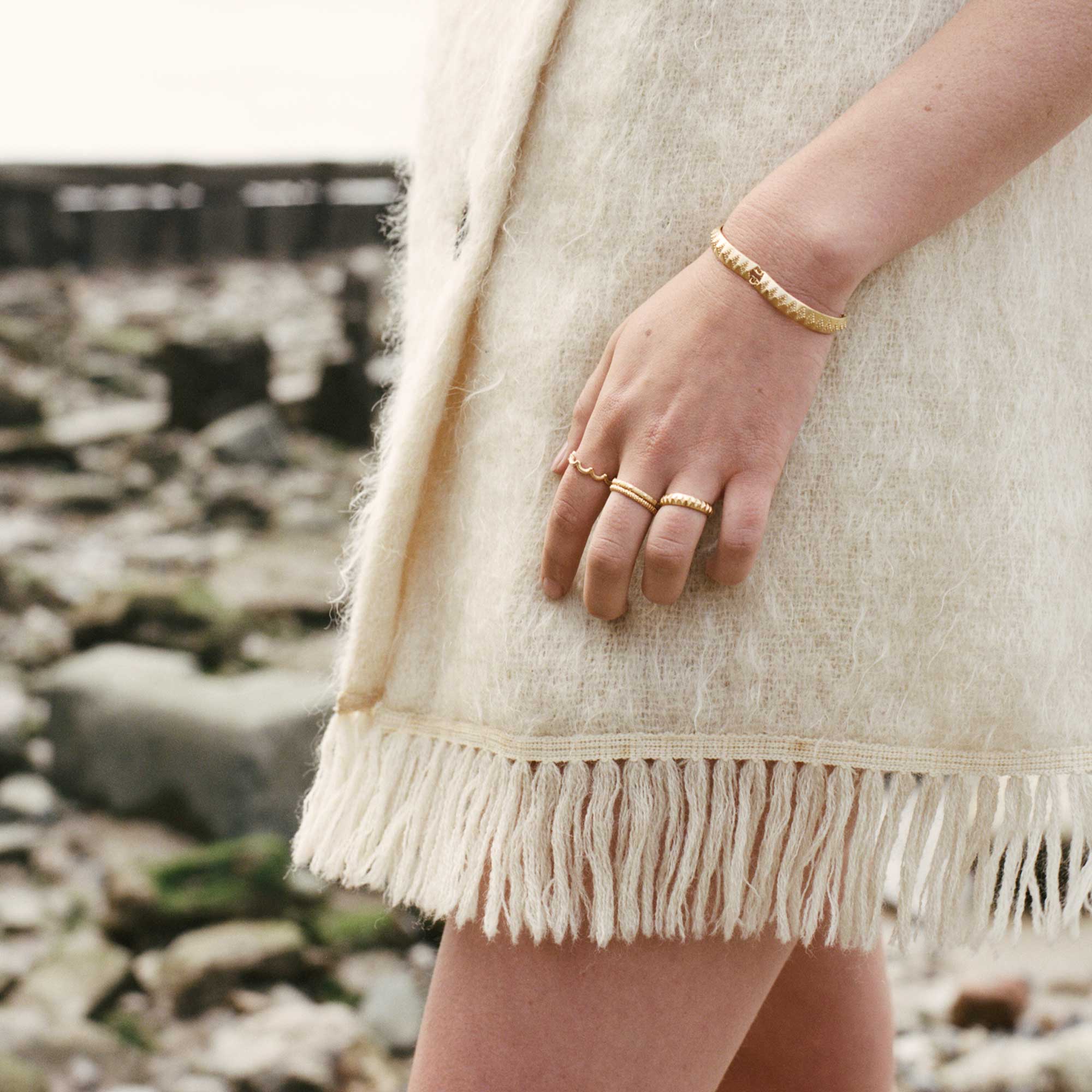 Model wearing gold hand jewellery on rocky beach