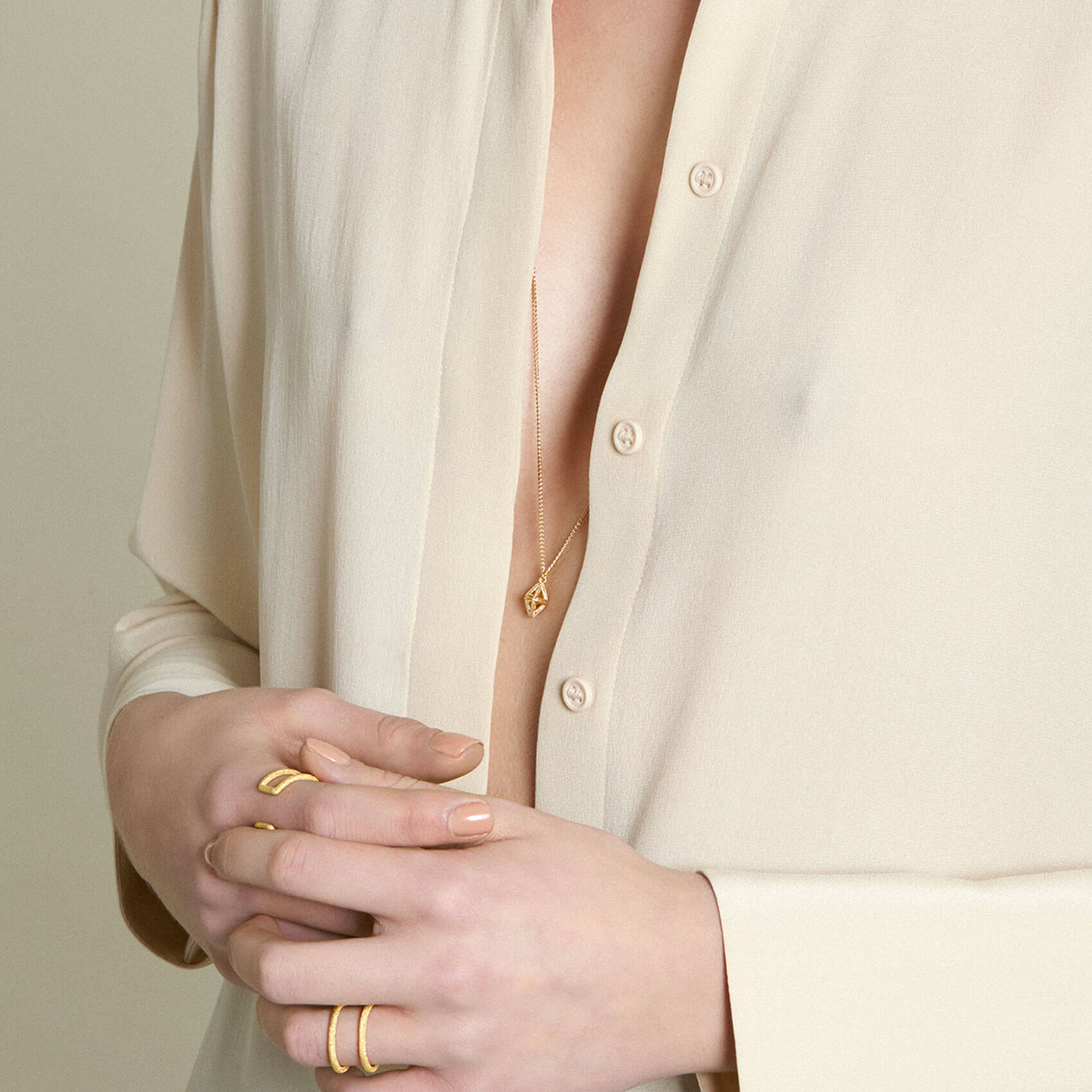 Model with opened blouse wearing octahedron shaped gold pendant necklace