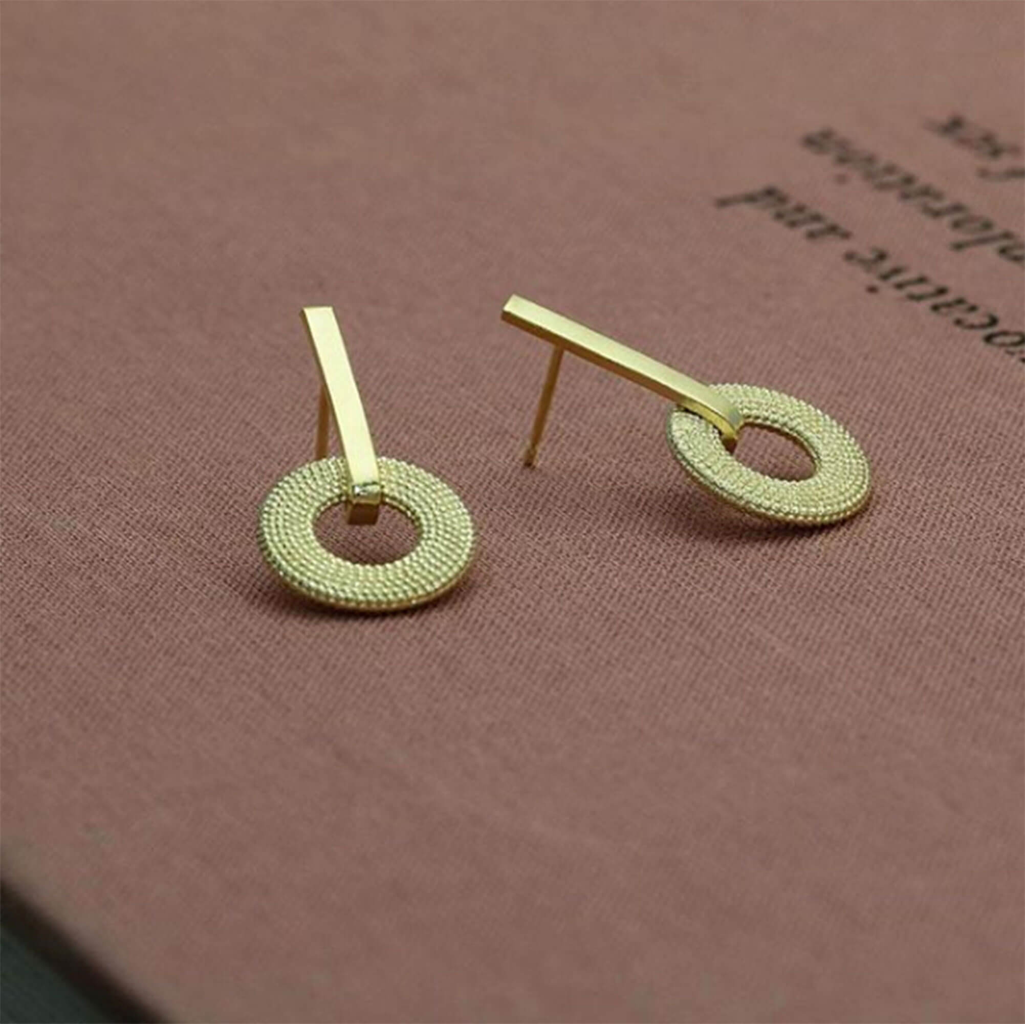 A pair of Weol Yellow Gold Drop Earrings on pink fabric