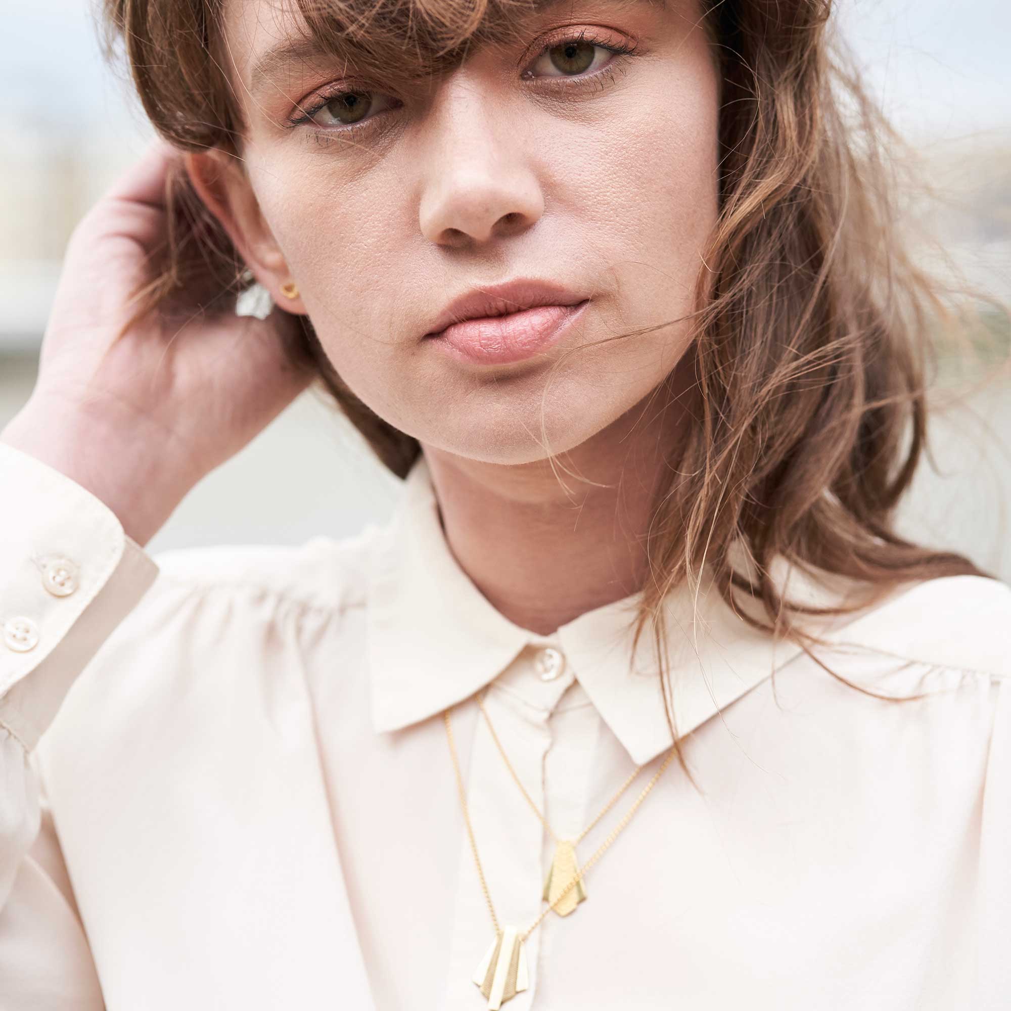 2 gold geometric pendant necklaces worn by model