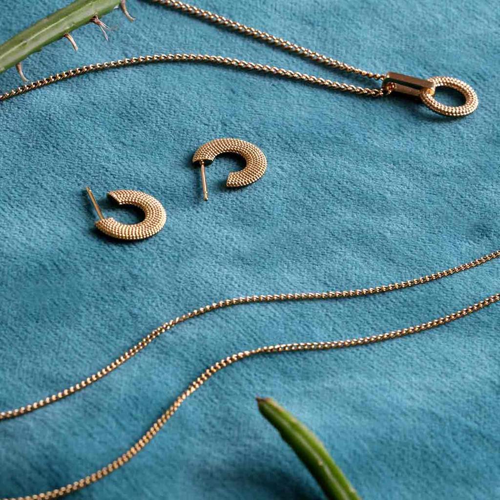 Textured gold huggie hoops surrounded by necklace