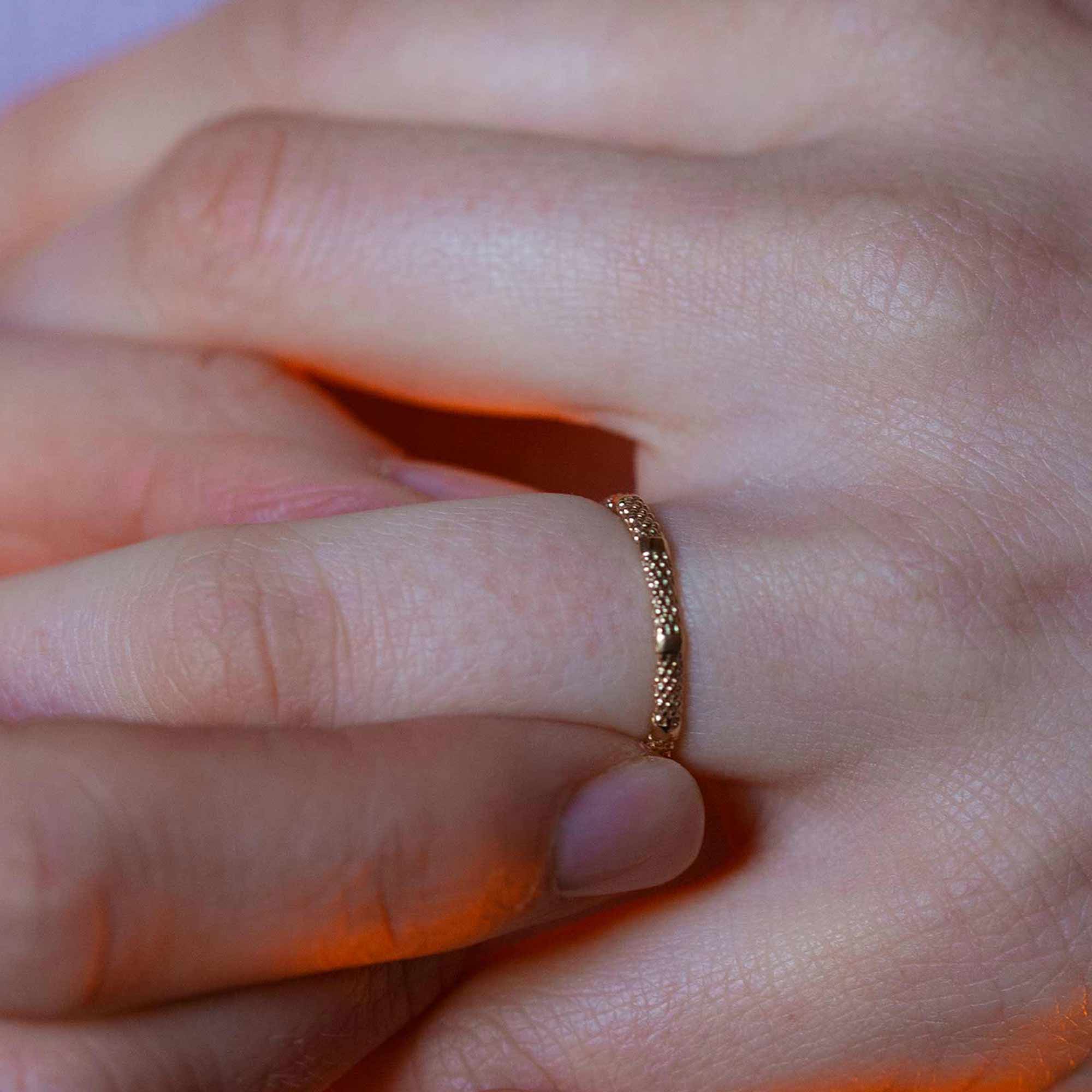 A slim rose gold stripy textured wedding ring is worn on models hand