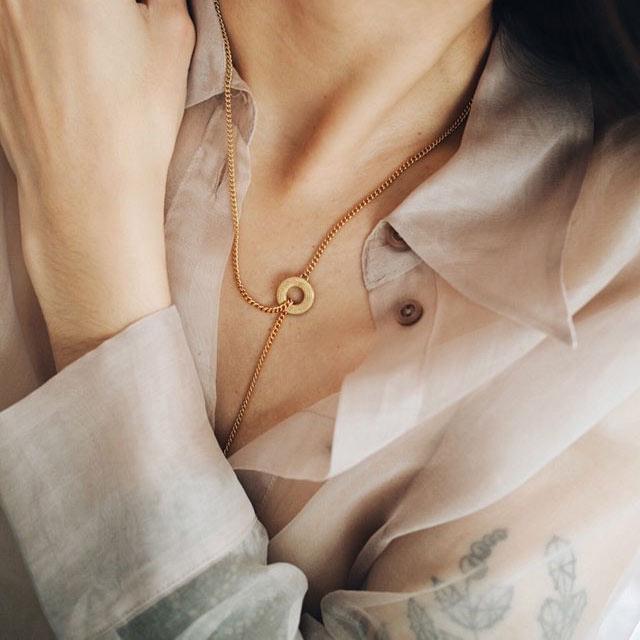 Model in see through blouse wearing gold chunky t bar necklace